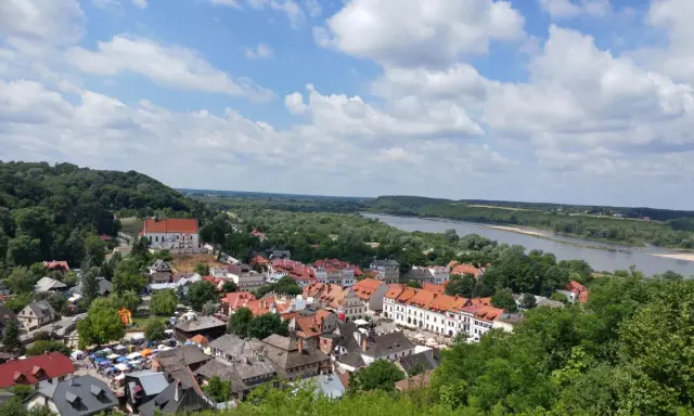 Widok na miasteczko z rzeką i lasami. W oddali widać wzgórze z krzyżami.