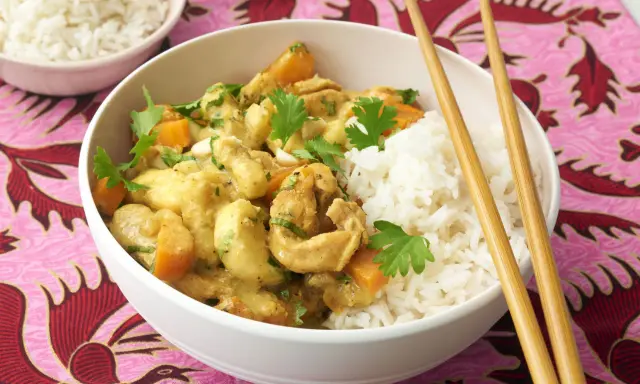 Ein köstliches Bananencurry mit Hähnchen, Karotten und Reis, garniert mit Koriander. Chopsticks liegen bereit.