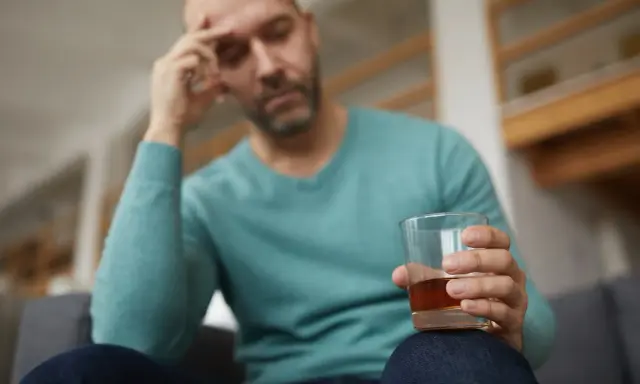 Mężczyzna z bólem głowy trzyma szklankę alkoholu, być może doświadczając reakcji disulfiramowej objawy.