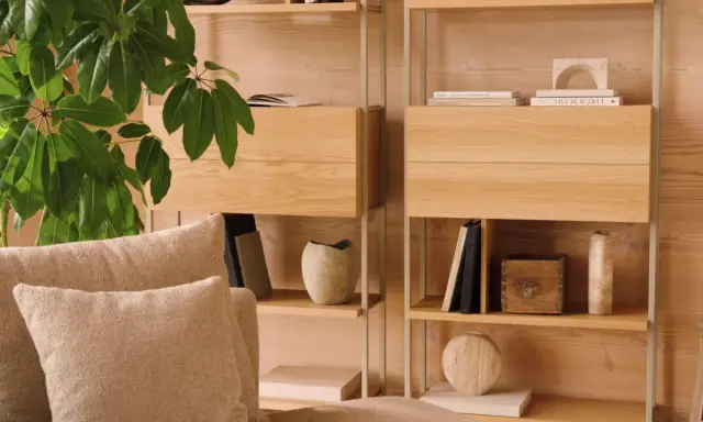 Mysig soffa med kuddar framför en hylla i ljust trä. Perfekt för dansk inredning inspiration med böcker och dekorativa föremål.