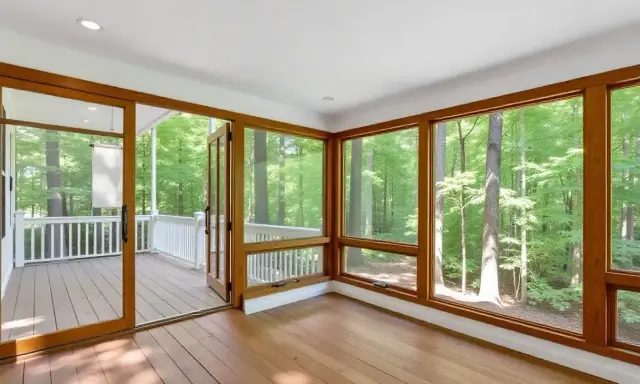 Amplio solárium con grandes ventanales y puertas de madera que dan a un porche. El color ventanas pvc de madera complementa el entorno boscoso.