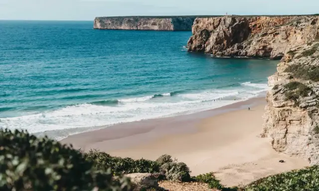Ein einsamer Surfer genießt die Wellen am Sagres Strand, umgeben von steilen Klippen und dem weiten Atlantik.