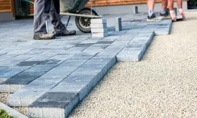 Układanie betonowych płyt na żwirze. Pracownicy tworzą ścieżkę, gdzie beton zamiast kostki staje się nowoczesnym rozwiązaniem.