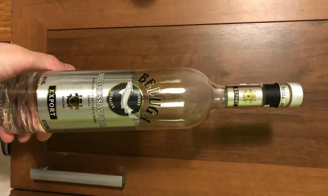 Butelka wódki Beluga Export, z etykietą "Noble Russian Vodka", leży na drewnianym blacie.