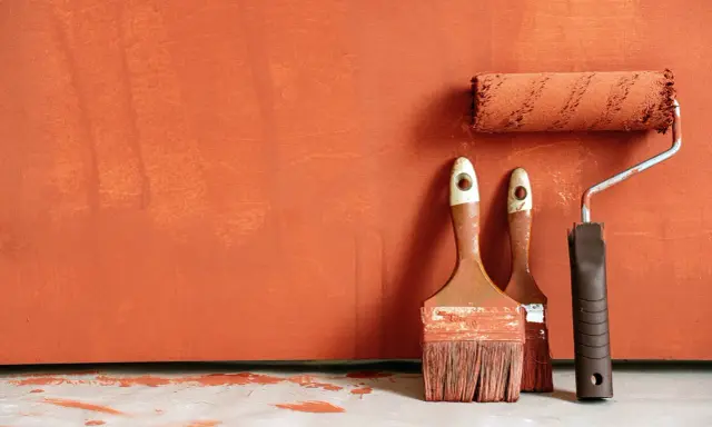 Deux pinceaux et un rouleau à peinture, prêts à rattraper trace de rouleau peinture sur un mur orange texturé.