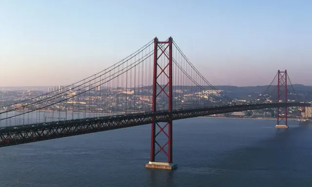 Der rote Hängebrücken-Gigant, oft als "Golden Gate Lissabon" bezeichnet, überspannt das ruhige Wasser mit der Stadt im Hintergrund.