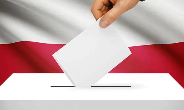 Dłoń wrzuca kartę do urny wyborczej na tle flagi Polski. To symbol ważnych wyborów do parlamentu.
