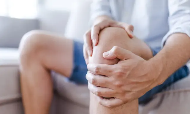 Mężczyzna trzyma się za kolano, odczuwając ból.