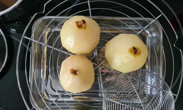 Trois poires pochées, prêtes pour une délicieuse recette tarte bourdaloue, égouttent sur une grille.