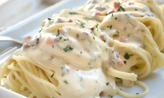 Cremige Spaghetti Carbonara mit Sahne, Speckwürfeln und Petersilie auf einem weißen Teller.