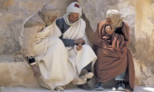 Drei Männer in traditioneller Kleidung sitzen und unterhalten sich. Sie diskutieren vielleicht, was haben Araber erfunden, während sie die Sonne genießen.