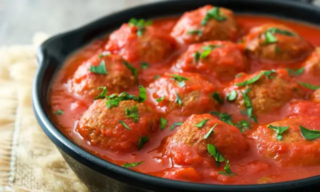 Polpette di carne succulente in salsa di pomodoro, guarnite con prezzemolo fresco, servite in una padella di ghisa.
