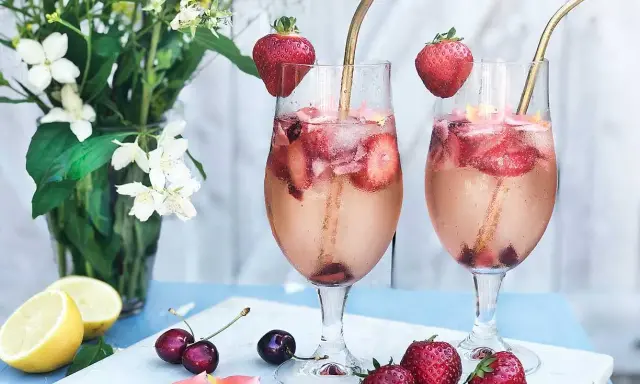 Två glas med drink med gin och prosecco, fyllda med is, jordgubbar och körsbär. Garnerade med jordgubbar och serverade med blommor och citron.
