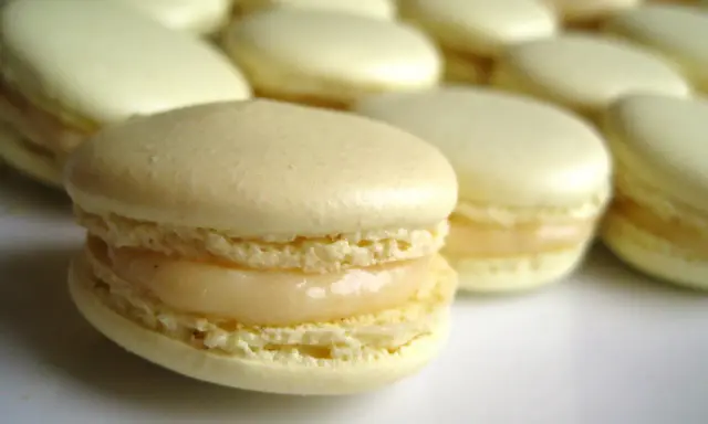 Un délicieux macaron meringue française, à la garniture crémeuse, se tient au premier plan, entouré d'autres macarons pâles.