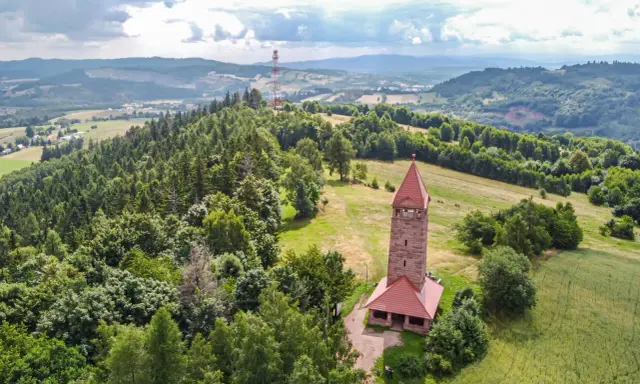 Kamienna wieża widokowa na wzgórzu, otoczona lasami i polami. Jedna z wielu wież widokowych na Dolnym Śląsku, oferująca malownicze krajobrazy.