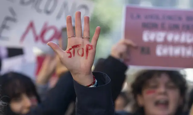 Mano alzata con "STOP" scritto in rosso, simbolo di protesta. Si evoca la necessità di una **codice rosso procedura** per proteggere le vittime.