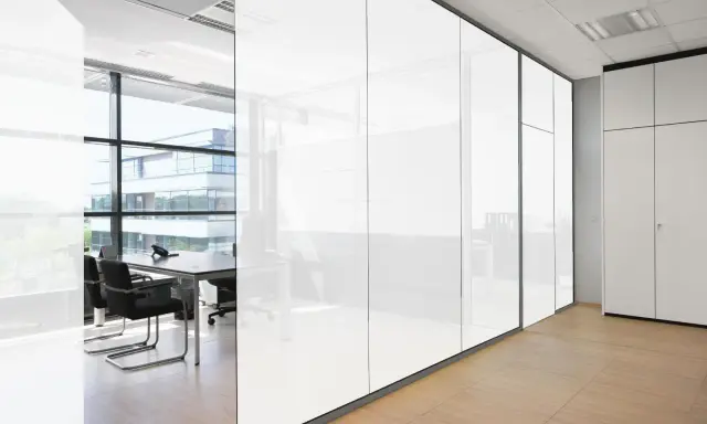 Oficina moderna con paredes de cristal que se oscurece, reflejando un edificio exterior y mobiliario de oficina.