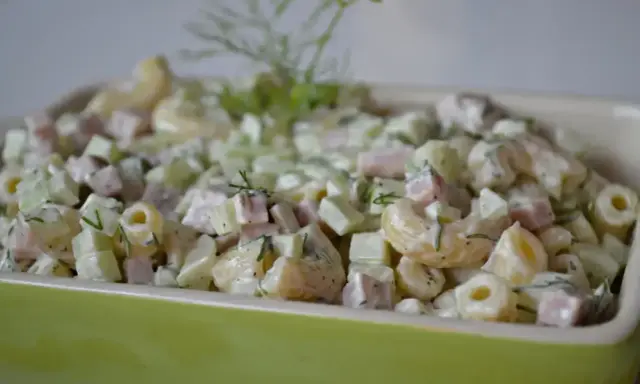 Pyszna sałatka z makaronem, szynką, ogórkiem i serem, udekorowana świeżym koperkiem.