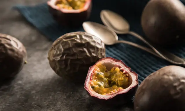 Reife Passionsfrüchte, eine aufgeschnitten, zeigen ihr saftiges Inneres. Zwei Löffel liegen bereit, um die exotische Frucht zu genießen.