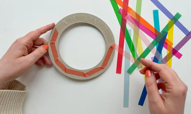 Hände bereiten einen Ring für Fenstersterne vor, indem sie bunte Streifen zum Falten bereitlegen.