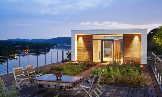 Moderner dachgarten auf einem Flachdach mit Blick auf einen See. Holzdeck, Sitzgelegenheiten und üppige Bepflanzung laden zum Entspannen ein.
