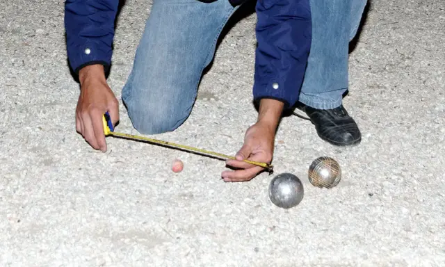 Un joueur de pétanque mesure la distance entre les boules. On se demande combien gagne un joueur de pétanque professionnel.
