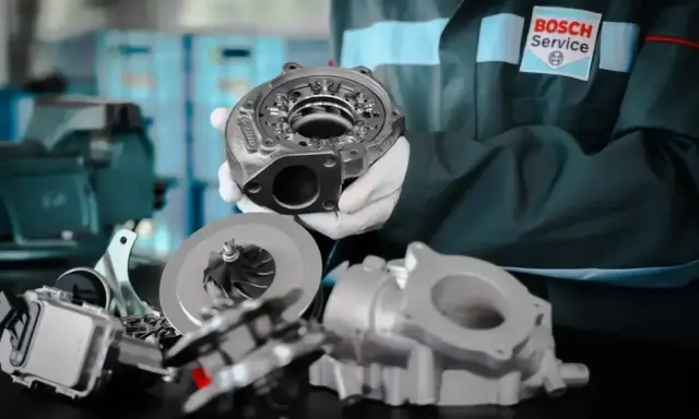Mechanik w rękawiczkach prezentuje części turbosprężarki. Dowiedz się, ile kosztuje regeneracja turbiny w Bosch Service.