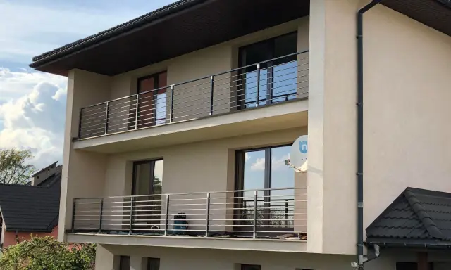 Nowoczesny dom z dwoma balkonami, gdzie zamiast tradycyjnej balustrady zastosowano elegancki murek z poziomymi stalowymi elementami.