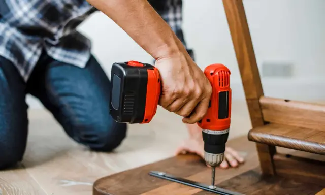 Un homme assemble un meuble en bois avec une perceuse. Un projet de bricolage maison réussi.