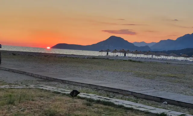Zachód słońca nad morzem w Czarnogórze w czerwcu. Idealna pogoda na plażowanie, z górami w tle i rzędem parasoli.