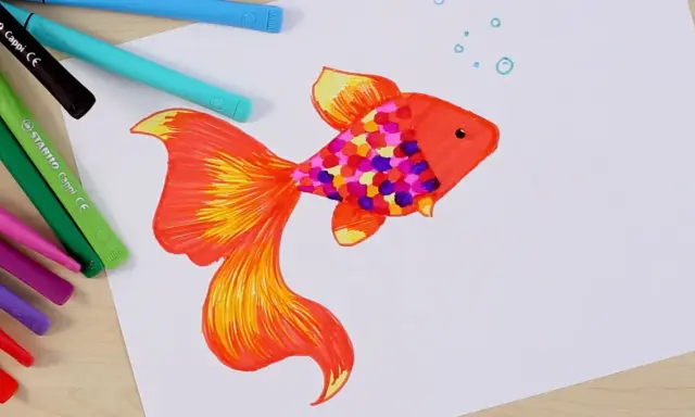Bunter Fisch mit bunten Schuppen, inspiriert von der Frage: was soll ich malen kinder. Buntstifte liegen daneben.