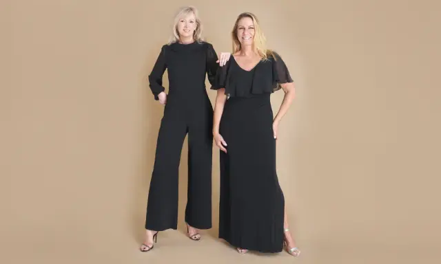 Two women in elegant black evening attire, a wide-leg jumpsuit and a flowing gown, ready for a formal event.