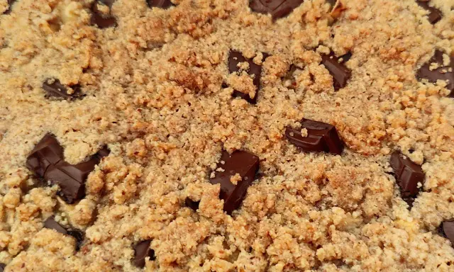 Gros plan sur un délicieux crumble pomme amande parsemé de morceaux de chocolat noir fondants.