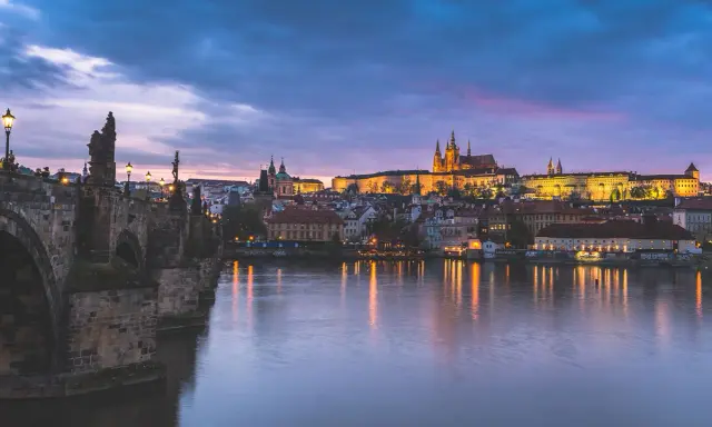 Nastrojowa fotografia nocna Pragi: Most Karola i Zamek na Hradczanach w blasku świateł, odbijających się w Wełtawie.