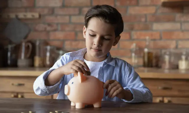 Niño introduce una moneda en una hucha rosa, aprendiendo sobre el ahorro con la cuenta infantil BBVA.
