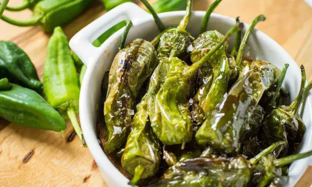 Friggitelli in padella, cotti e lucidi, cosparsi di sale grosso, in una ciotola bianca.