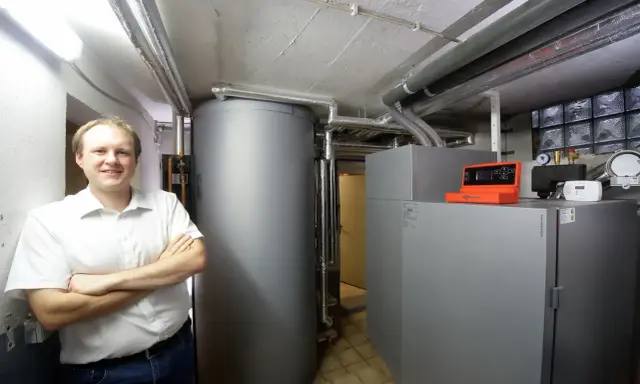 Mann vor Pelletheizung und großem Speicher in Heizungsraum.