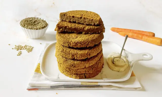 Impilati hamburger di lenticchie dorati, con lenticchie secche, carote e una salsa cremosa in un piatto.