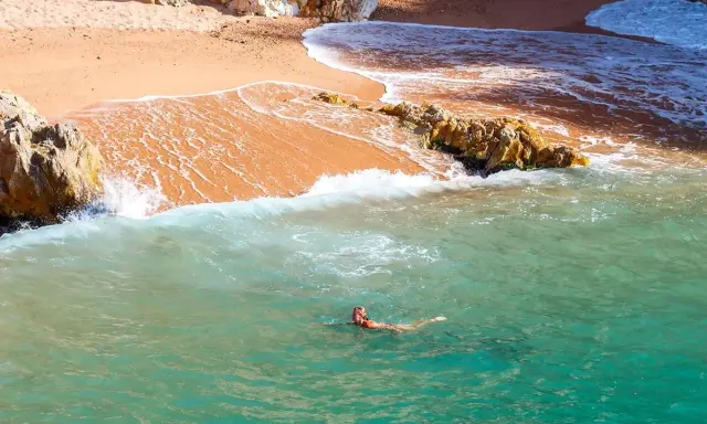 Eine Frau schwimmt im türkisfarbenen Meer vor einer sandigen Bucht in Palamós, Spanien.