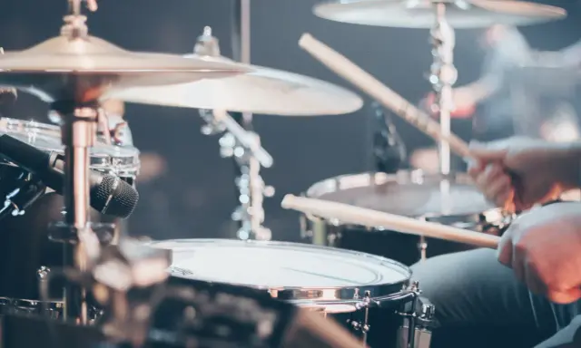 Gros plan sur un set de batterie, avec des baguettes en action. Différents types de tambour et cymbales sont visibles.