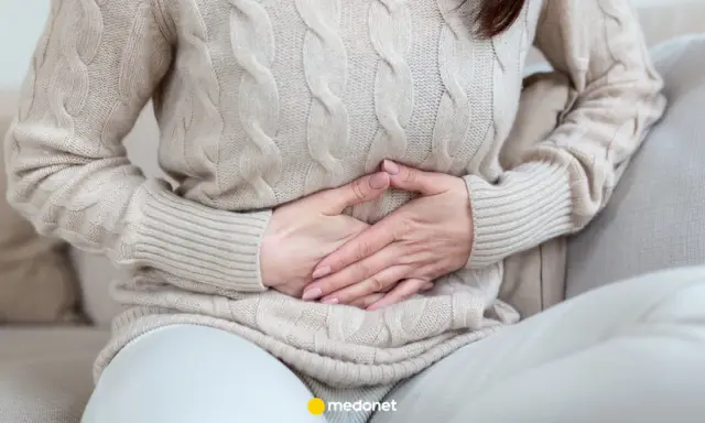 Kobieta trzyma się za brzuch, odczuwając ból brzucha po jedzeniu.