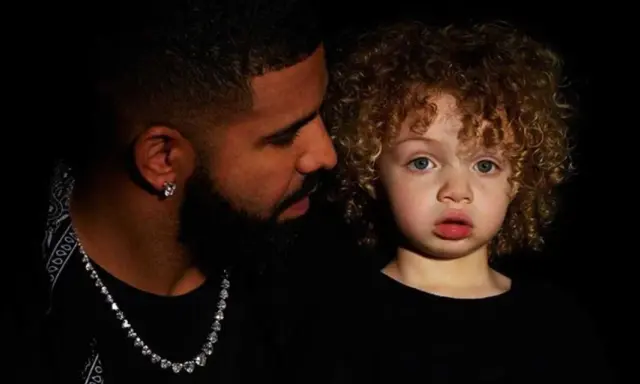 Drake i jego syn, Adonis, w czarnych ubraniach. Chłopiec ma kręcone, jasne włosy i niebieskie oczy.