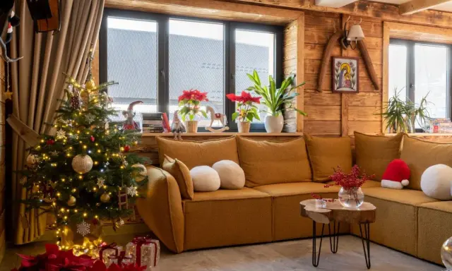 Przytulny salon z choinką i prezentami, tworzący atmosferę **świąt w górach**. Drewniane ściany i okna dodają uroku.