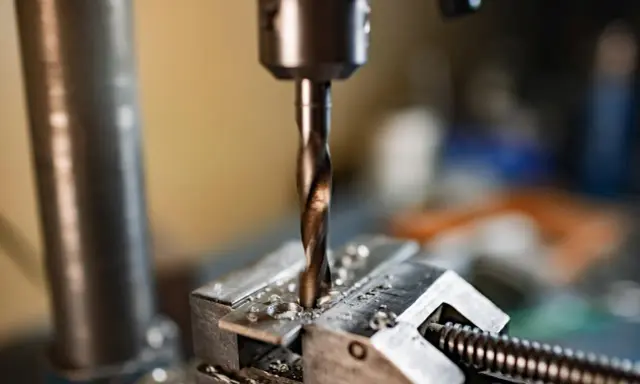 Wiertło wkręca się w metalowy element przytrzymywany przez imadło.