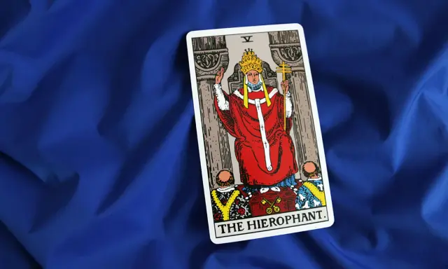 Karta Tarota "The Hierophant" na niebieskim tle. Postać w czerwonych szatach z tiarą i krzyżem.