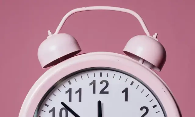 Różowy budzik z dzwonkami. Wskazówki pokazują godzinę 12:21. To znaczenie czasu, który ucieka.