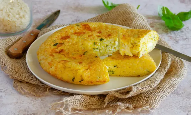 Una gustosa frittata di riso dorata, con erbe aromatiche, servita su un piatto bianco con una fetta tagliata.