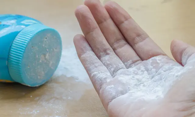 Mano con borotalco bianco sparso, vicino al contenitore blu. Attenzione: il borotalco è cancerogeno.