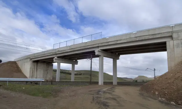Un puente de hormigón cruza vías de tren. Los pilares de soporte, que son un estribo, sostienen la estructura. El cielo está nublado.