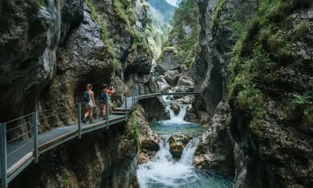 Due escursioniste attraversano passerelle metalliche nel suggestivo orrido di Uriezzo, con un fiume impetuoso che scorre tra le rocce.